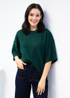 Woman wearing a green sweater and dark jeans against a white background