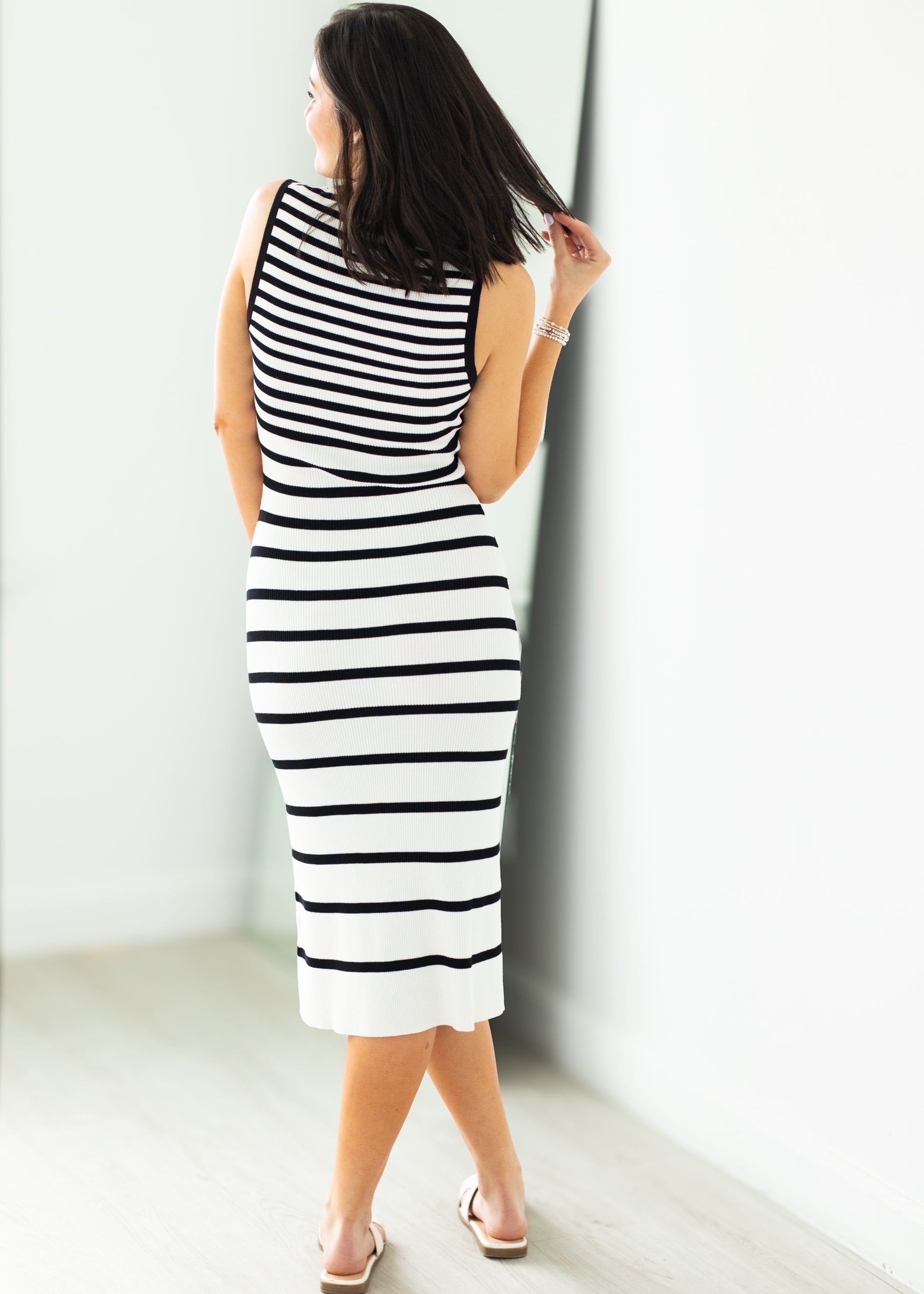 Woman wearing a black and white striped dress against a white wall.