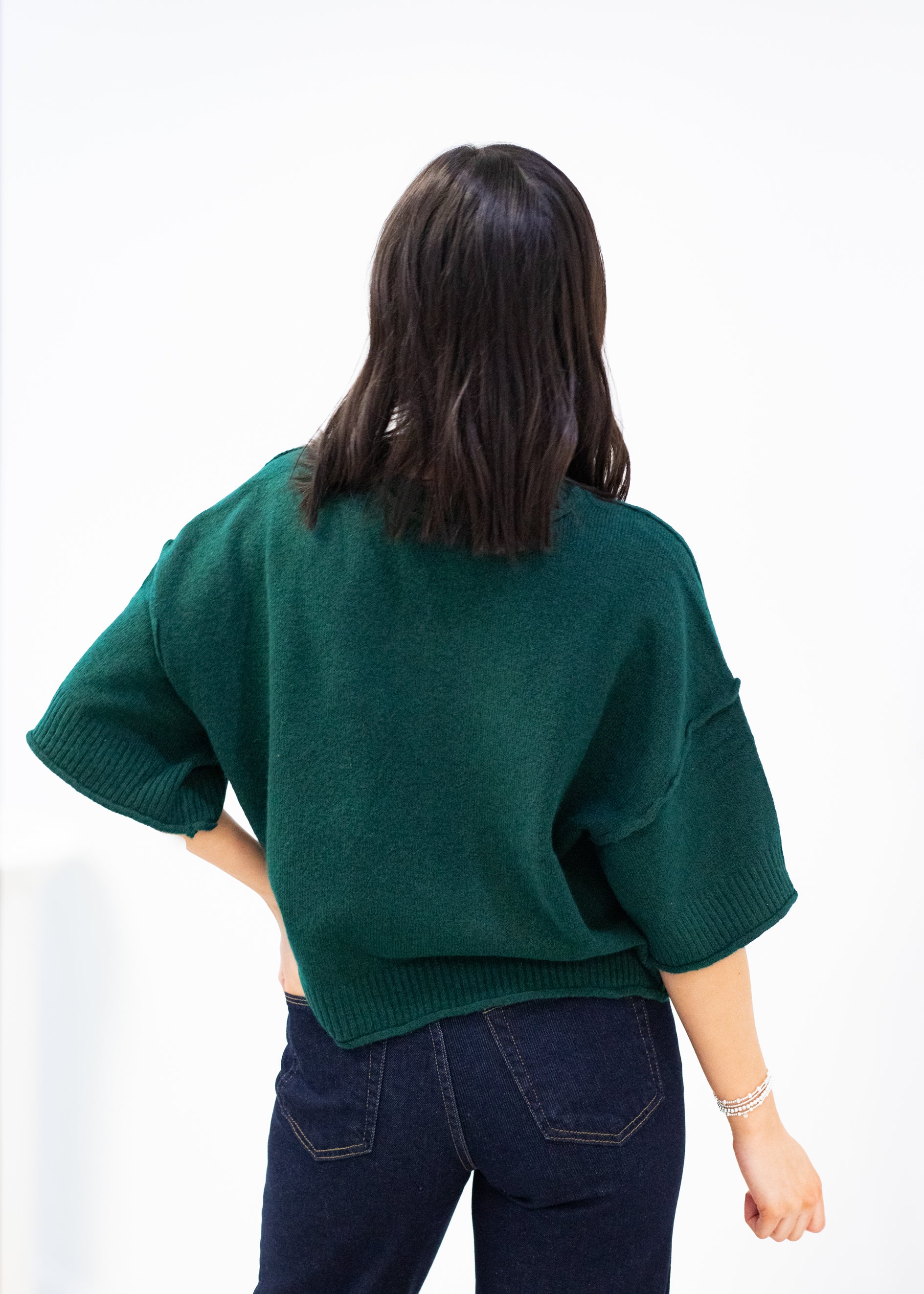 Person wearing a green sweater and dark jeans on a white background