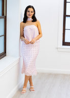Woman wearing a strapless pink dress with white lace details in a bright room.