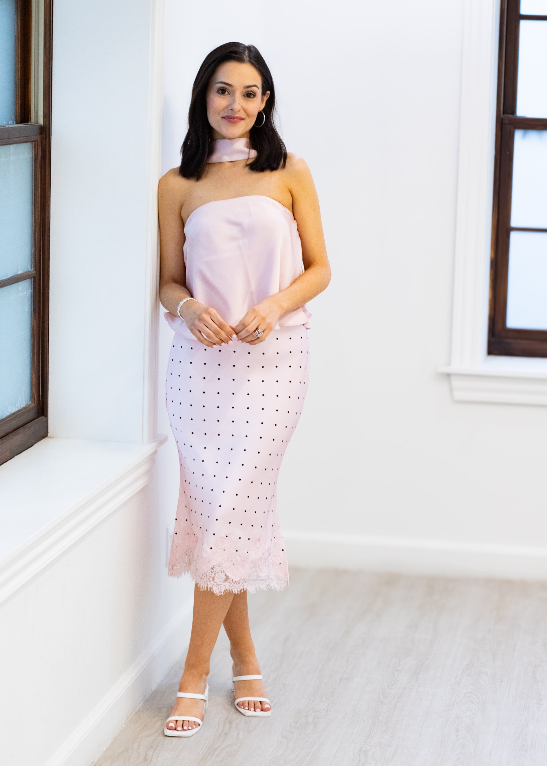 Woman wearing a strapless pink dress with white lace details in a bright room.