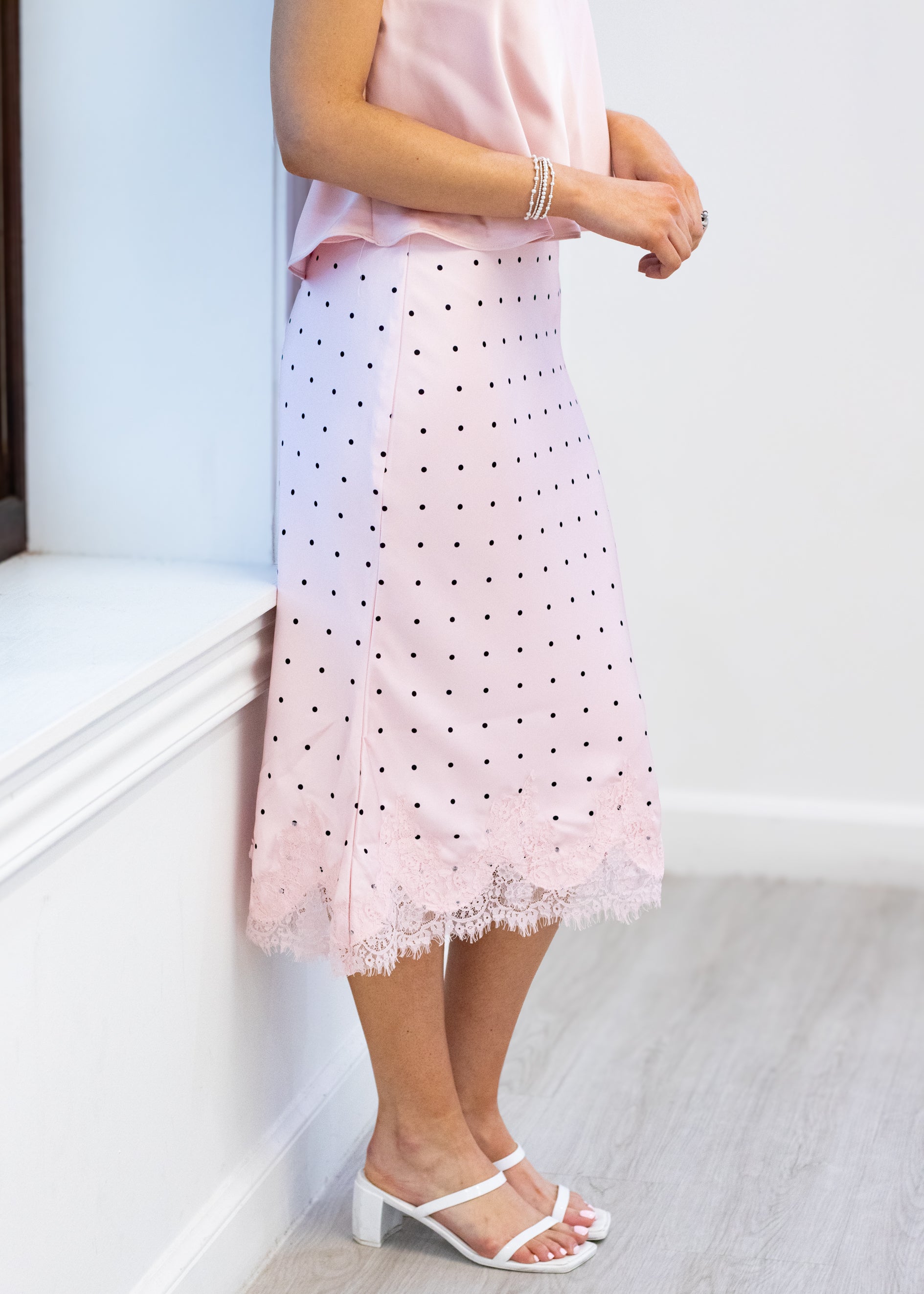 Person wearing a pink lace skirt with black polka dots on a white background