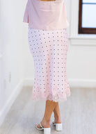 Person wearing a light pink top and polka dot skirt in a minimal indoor setting.