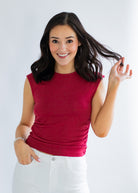 Woman wearing a red sleeveless top and white pants against a plain background