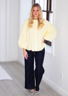 Woman wearing a light yellow blouse with ruffled sleeves on a gray background