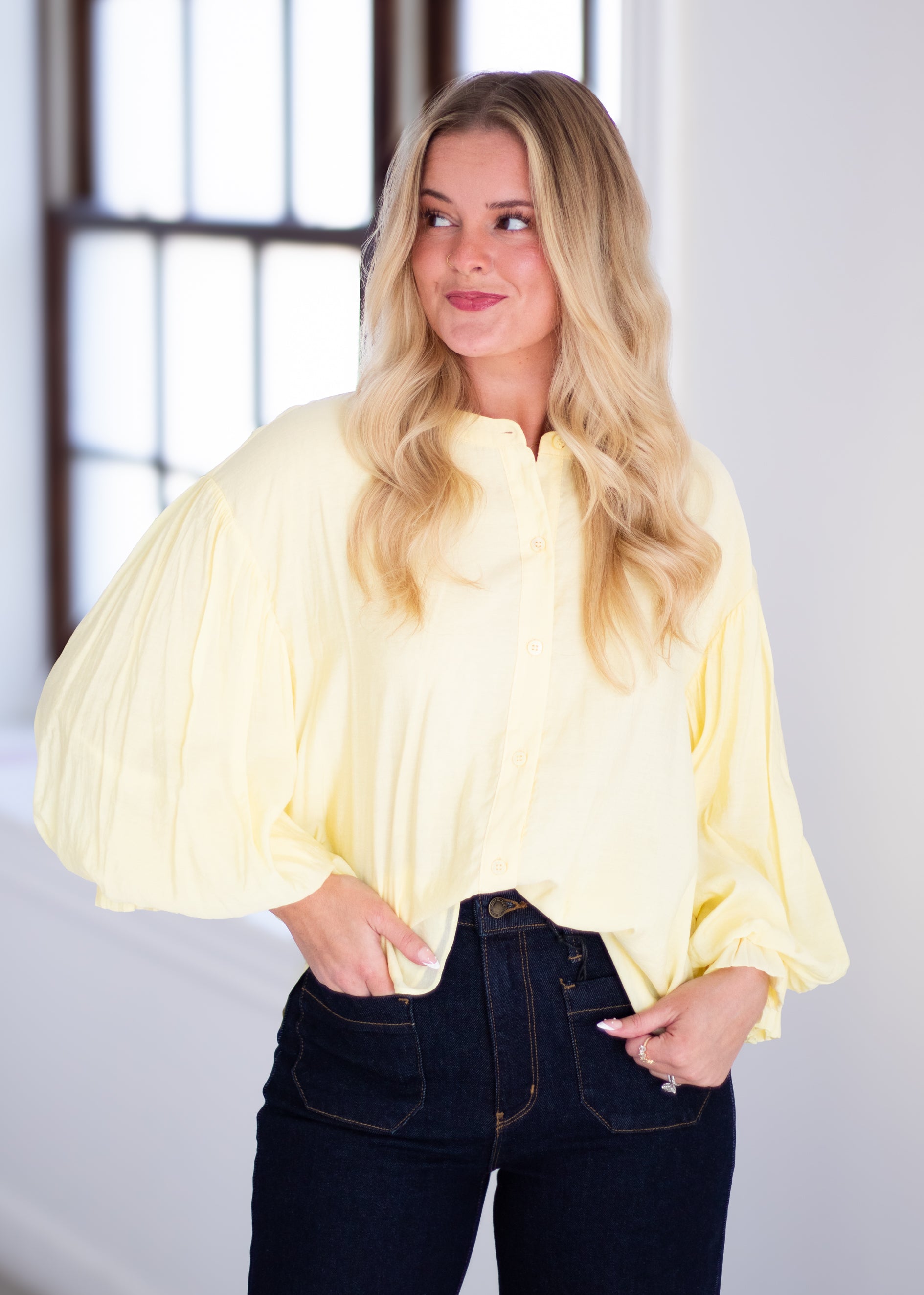 Woman wearing a light yellow blouse with ruffled sleeves on a gray background