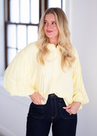 Woman wearing a light yellow blouse with ruffled sleeves on a gray background