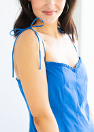 Woman wearing a blue sleeveless top with thin straps on a white background