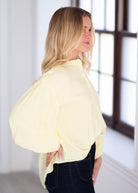 Woman wearing a light yellow blouse with ruffled sleeves on a gray background