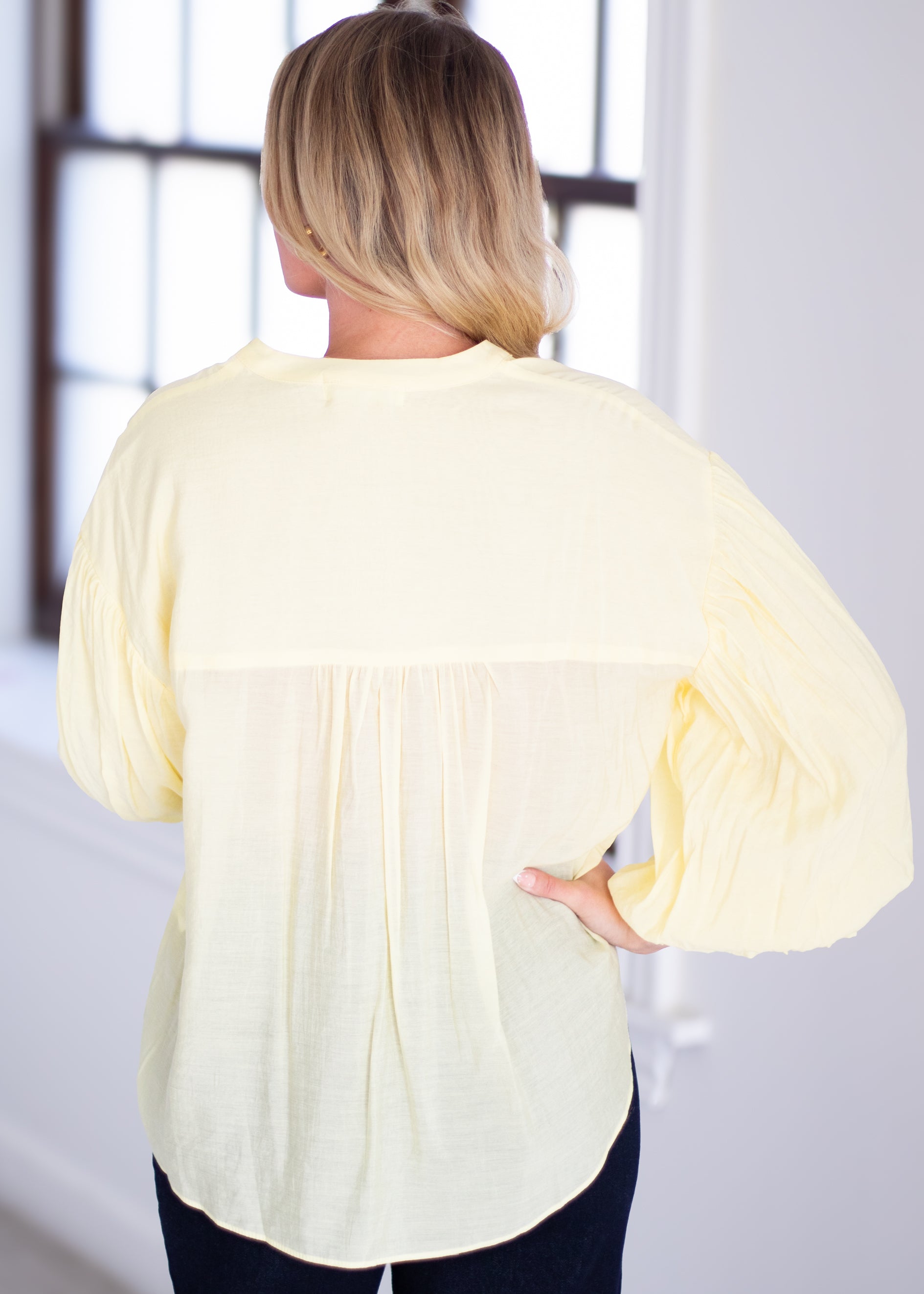 Woman wearing a light yellow blouse with ruffled sleeves on a gray background