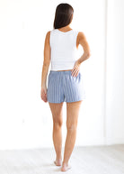 Woman wearing a white sleeveless top and blue striped shorts on a white background