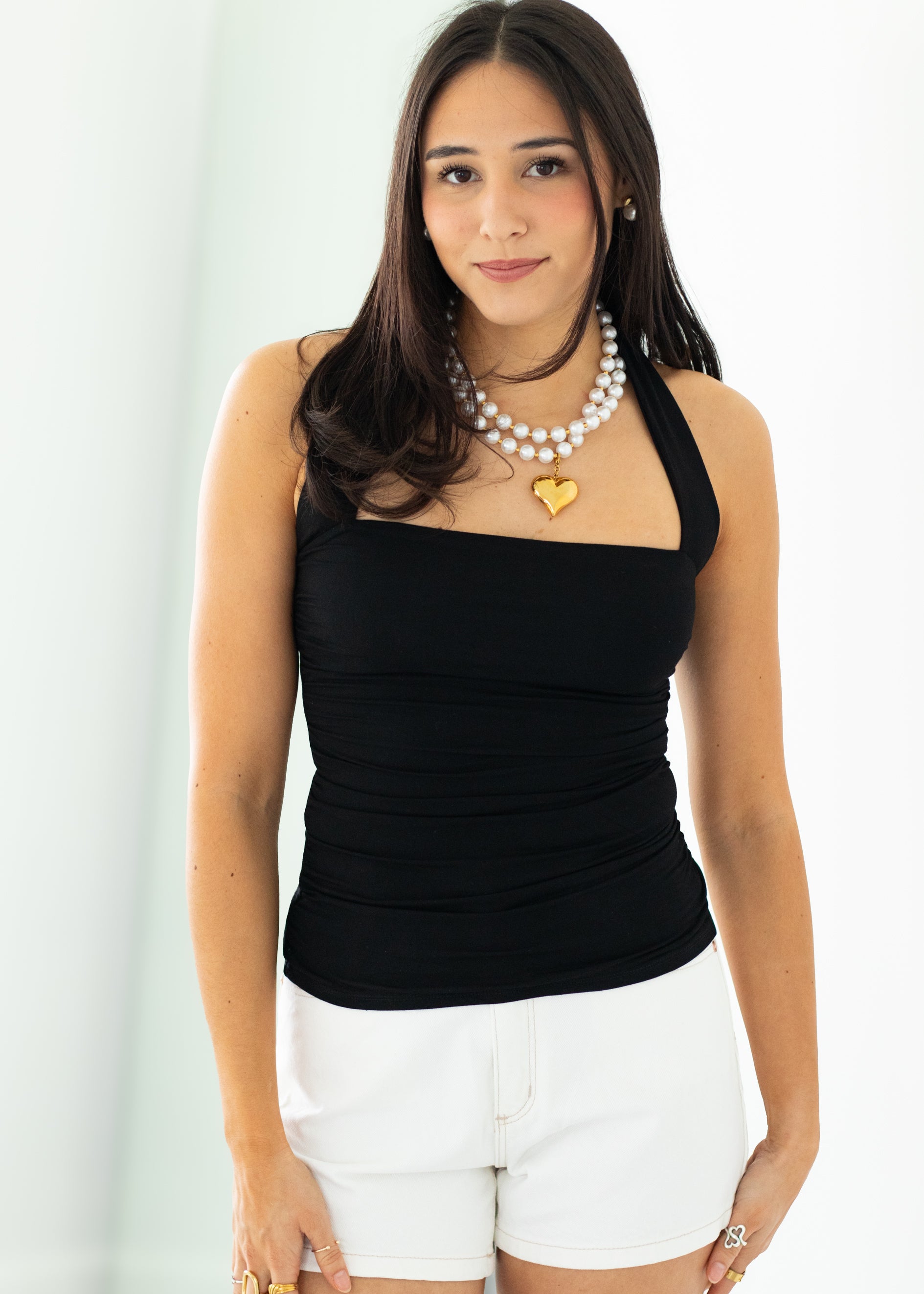 Woman wearing a black top and white shorts with jewelry on a plain background