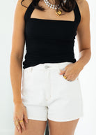 Person wearing a black tank top and white shorts with a plain background