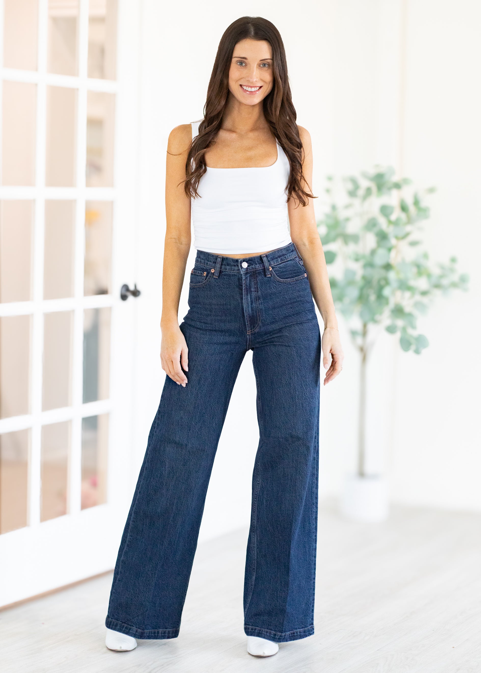 Woman wearing blue jeans and a white top in a bright room.
