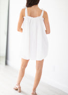 Woman wearing a white dress with floral embroidery on a plain background
