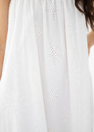 Woman wearing a white dress with floral embroidery on a plain background