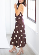A woman wearing a brown halter midi dress with large cream polka dots, standing in a bright room with white walls and a window.