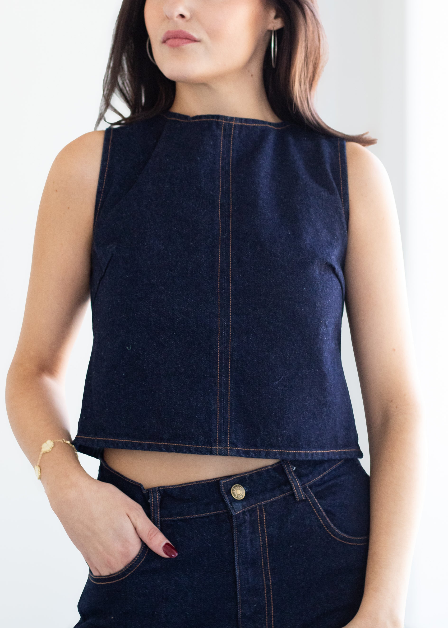 Person wearing a dark blue denim sleeveless top and jeans on a white background
