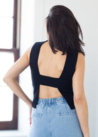 Woman wearing a black sleeveless top with open back and light blue jeans.