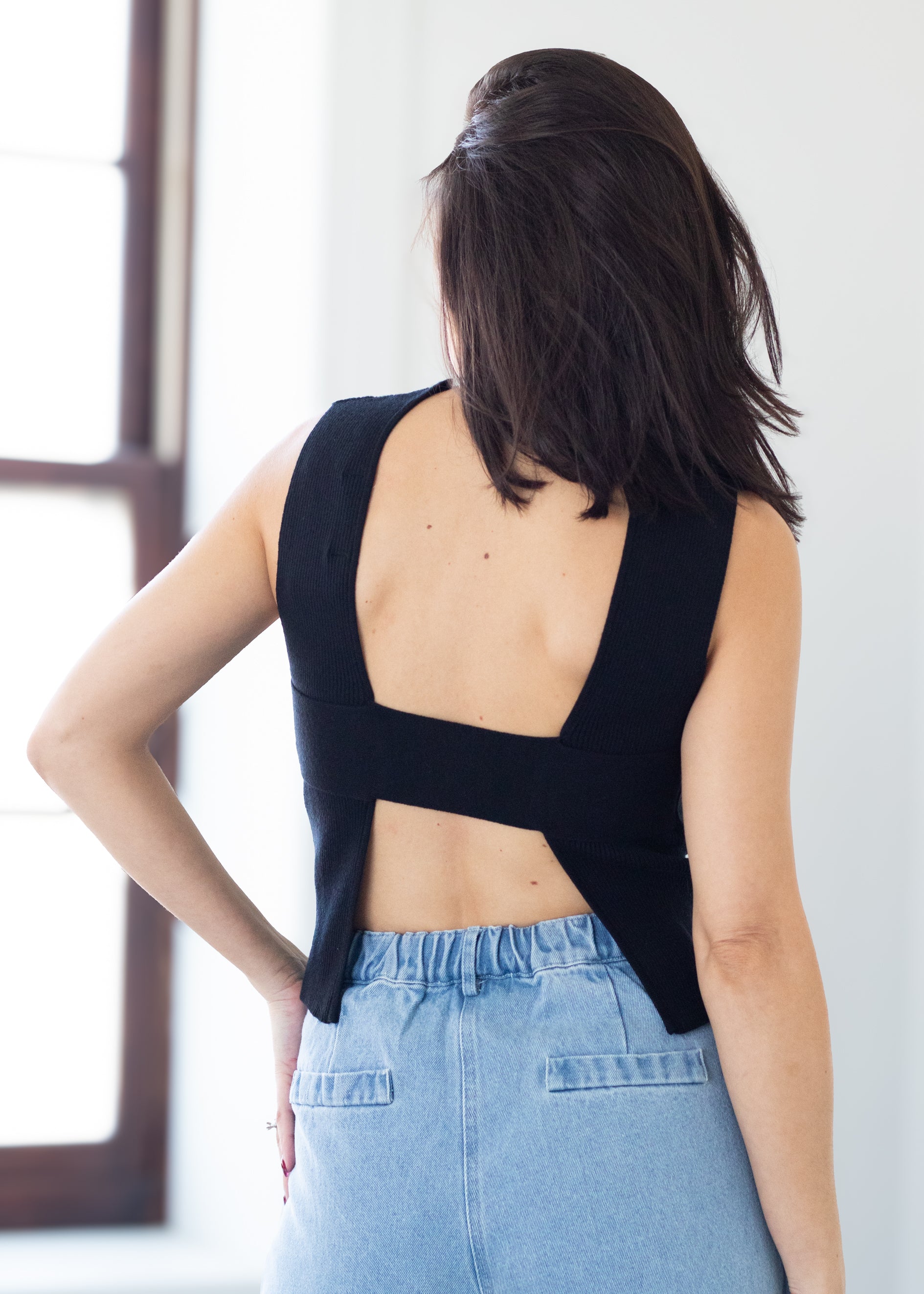 Woman wearing a black sleeveless top with open back and light blue jeans.