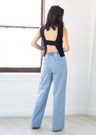 Person wearing a black sleeveless top and light blue jeans standing in a minimalistic room.