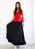 Woman wearing a red top and black pleated skirt on a white background