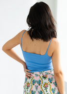 Woman wearing a blue tank top and floral skirt against a white background