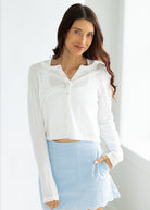 Woman wearing a white blouse and light blue skirt against a white background