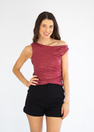 A woman modeling a sleeveless, off-the-shoulder top in a deep burgundy or maroon color, paired with black shorts, against a plain white studio background.