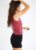 A woman wearing a sleeveless, zippered dusty rose leather-like top and black shorts, shown from a side-back angle against a plain white studio background.