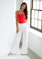 Woman wearing a red top and white wide-leg pants in a bright room.
