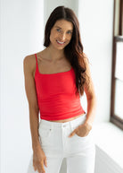 Woman wearing a red tank top and white pants indoors.
