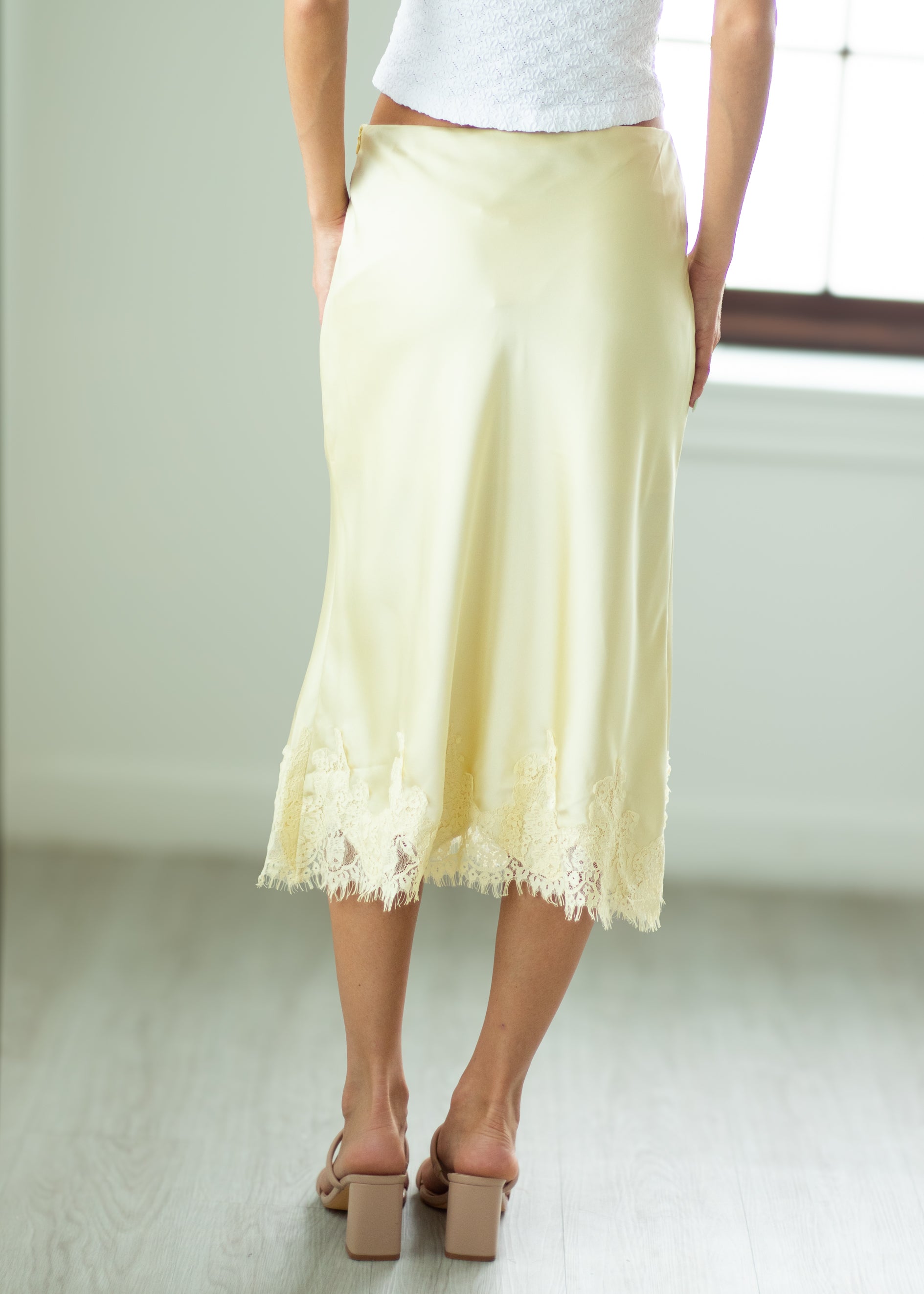 Person wearing a light yellow lace skirt with a white top and brown shoes on a plain background