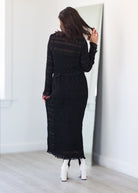 Woman wearing a black dress standing in front of a mirror.