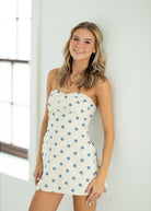 Woman wearing a strapless polka dot dress against a white wall.