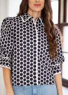 A woman wearing a navy and white polka dot button-up blouse with puff sleeves, paired with light blue jeans.