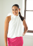 Woman wearing a white sleeveless top with a bow and a pink striped skirt indoors.