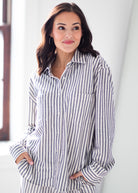 A woman wearing a long-sleeve button-up shirt with vertical navy and white stripes, standing in a brightly lit indoor setting.