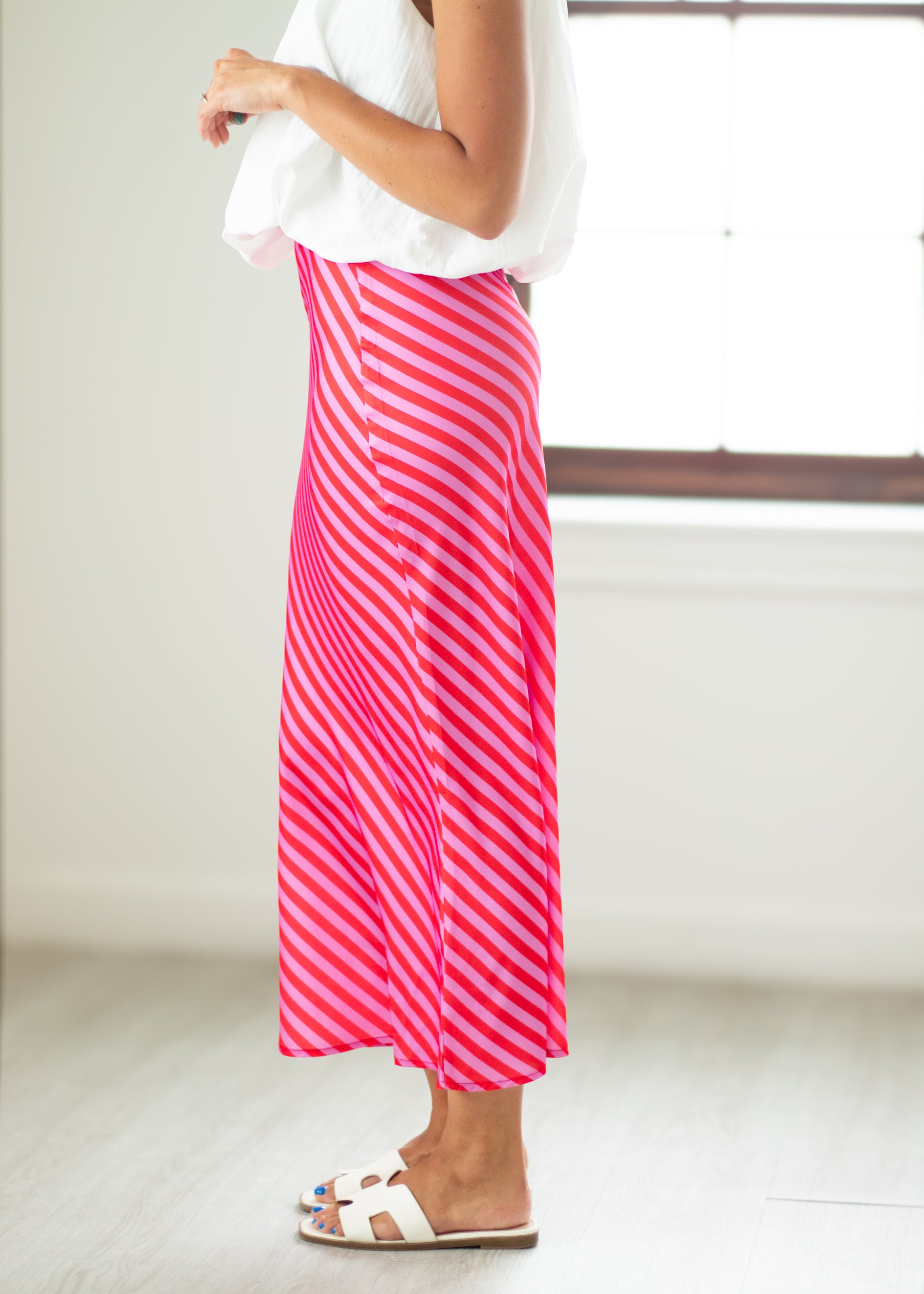 Person wearing a white top and pink striped skirt in a minimal indoor setting