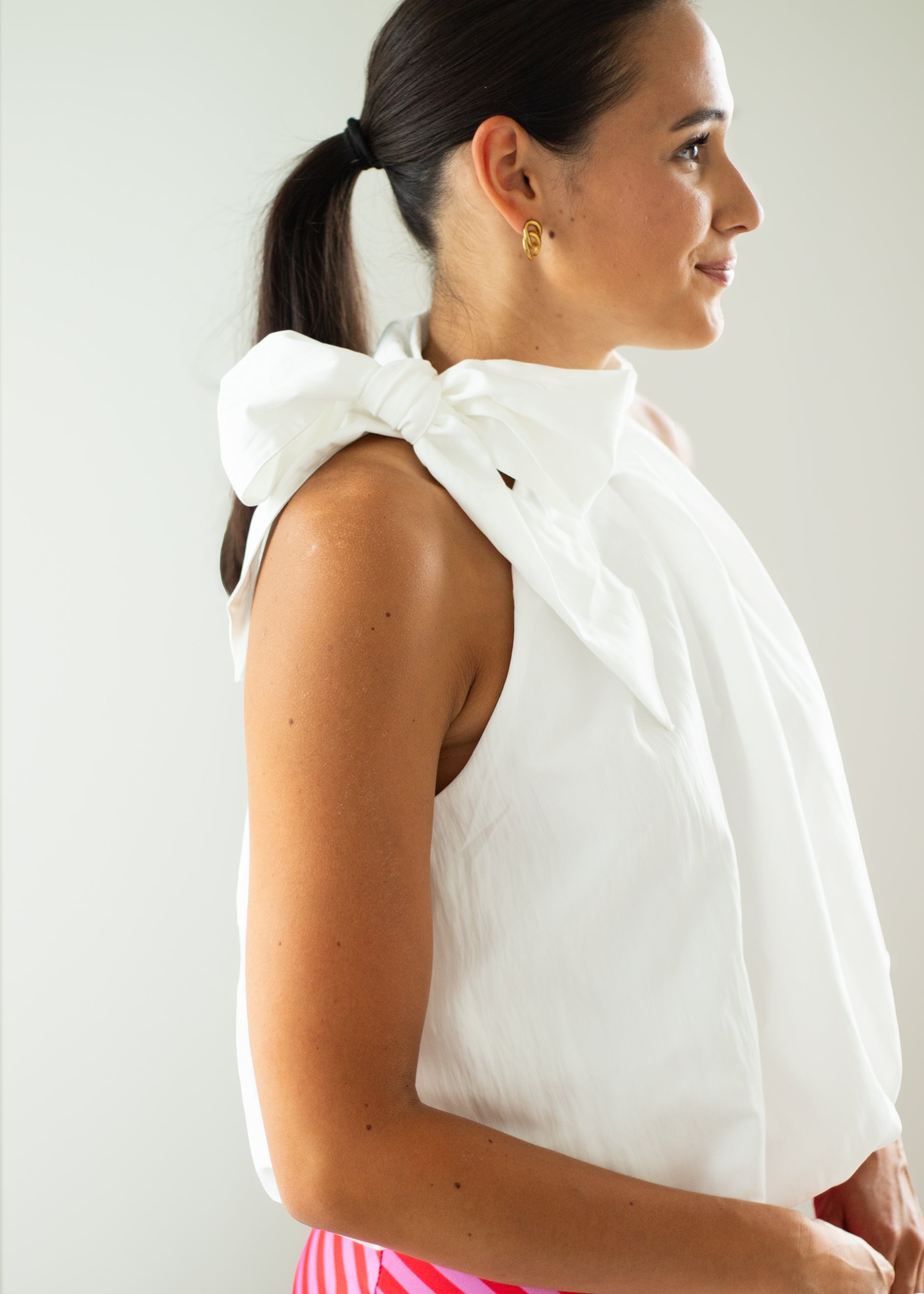 Woman wearing a white sleeveless top with a bow detail on a plain background