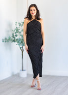 Woman wearing a black halter neck dress standing indoors with a white background