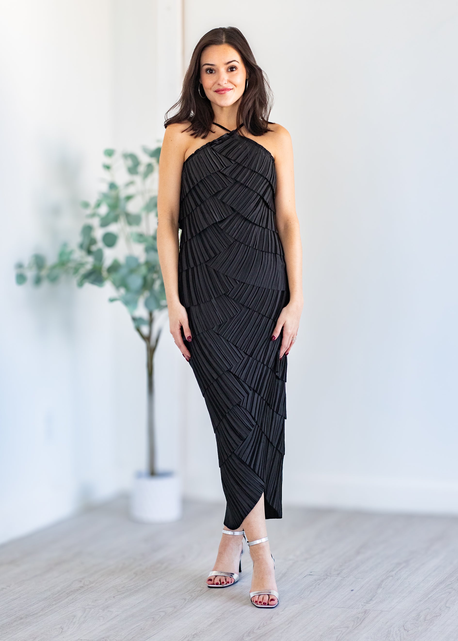 Woman wearing a black halter neck dress standing indoors with a white background