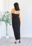 Woman wearing a black tiered dress in a minimal indoor setting with a plant.