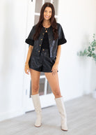 Woman wearing a black leather outfit with white knee-high boots in a bright room.