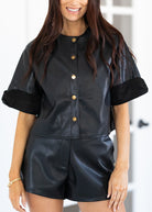Woman wearing a black leather outfit with gold buttons against a white background