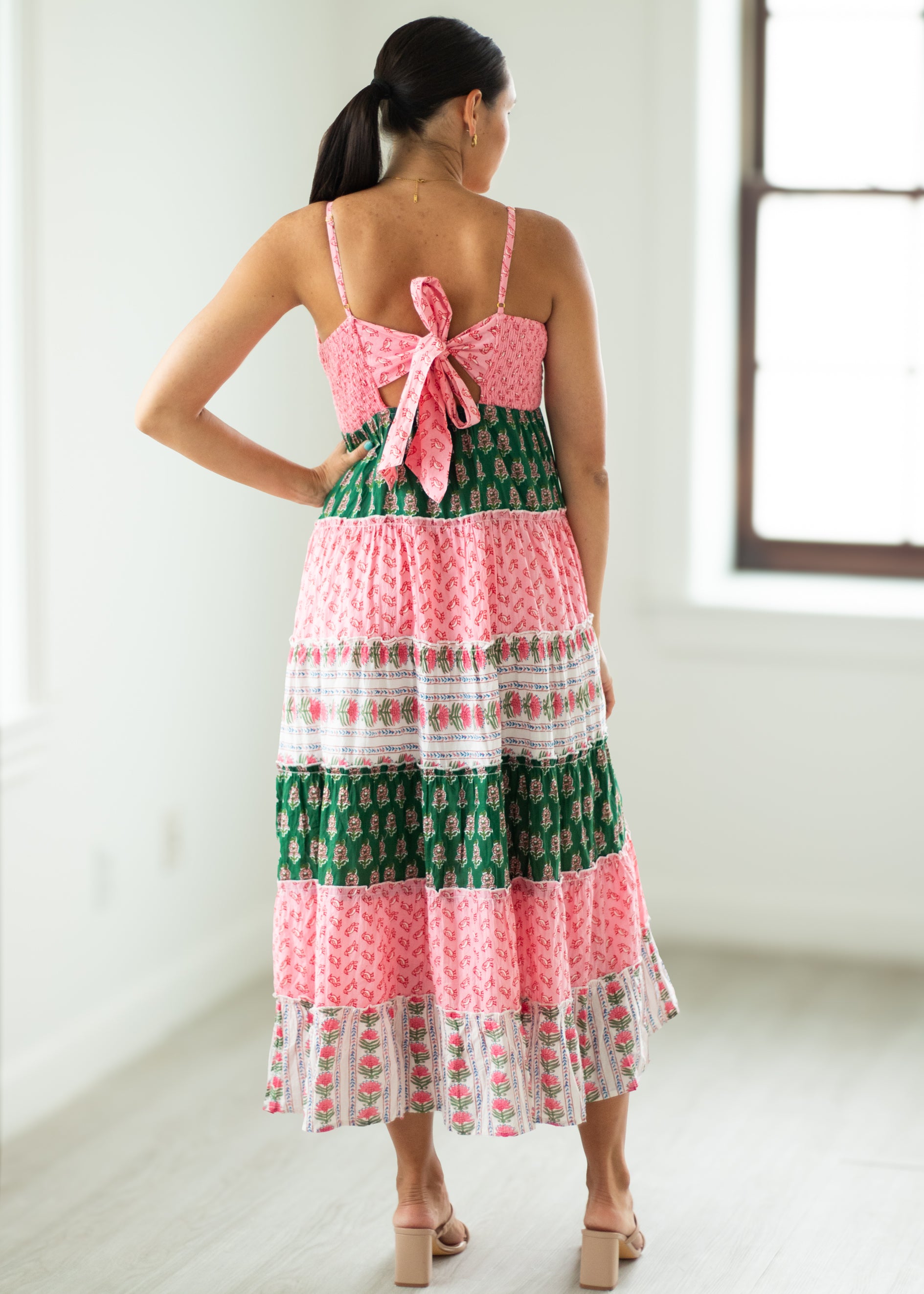 Woman wearing a colorful dress with a pink and green pattern in a bright room.