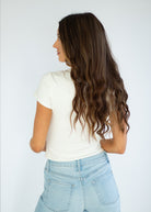 Woman with long wavy hair wearing a white t-shirt and light blue jeans against a plain background