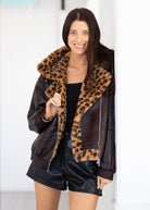 Woman wearing a brown leather jacket with leopard print fur collar against a white background