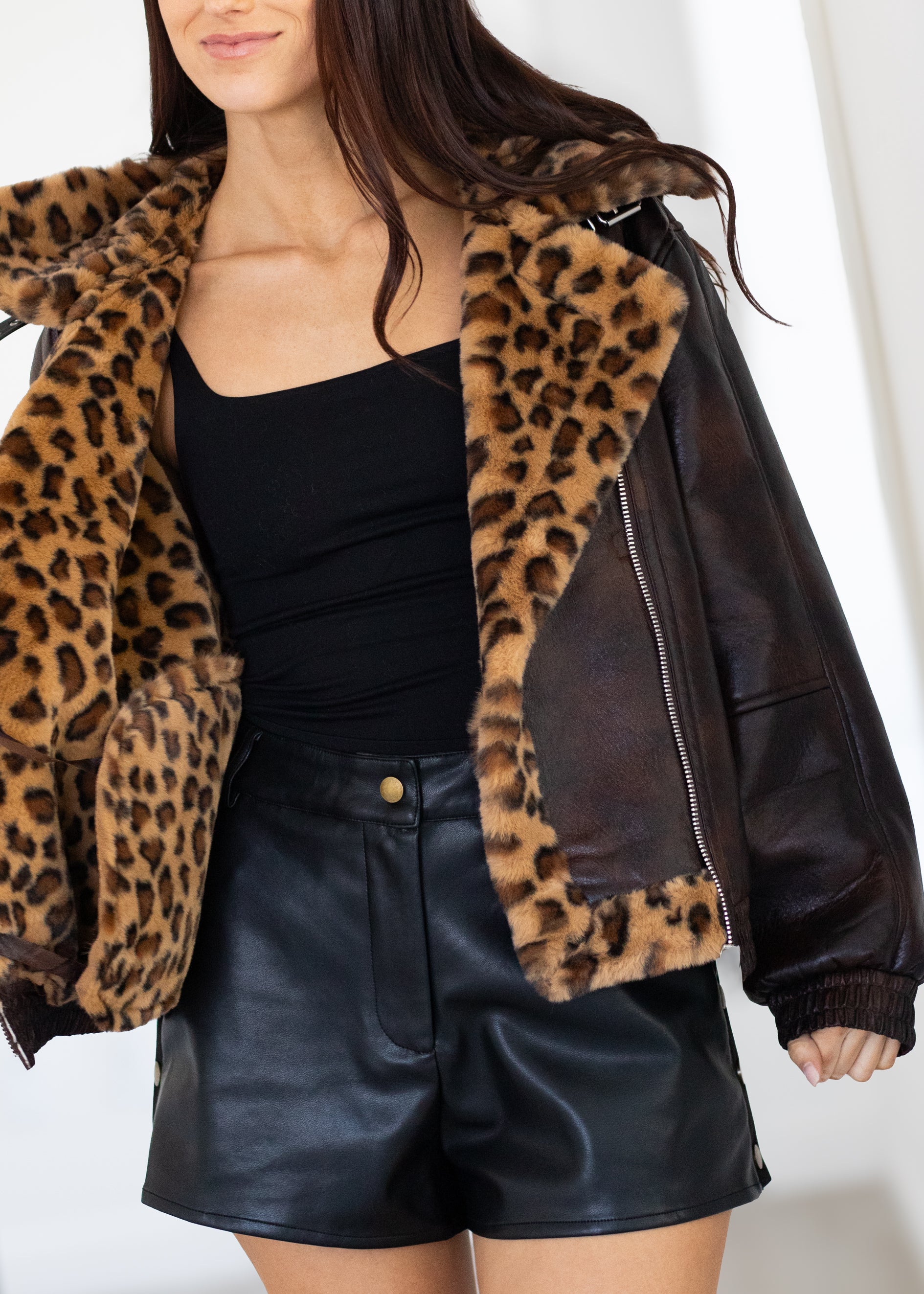 Person wearing a leopard print jacket with a black top and leather shorts on a white background
