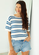 Woman wearing a blue and white striped shirt and denim shorts against a white background